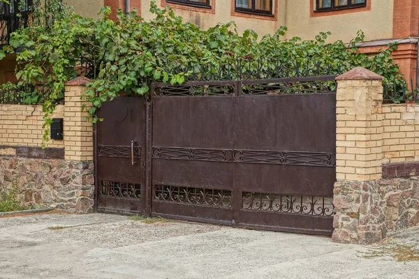 旧的棕色铁门和街道上绿色植被的砖栅栏 — 图库照片