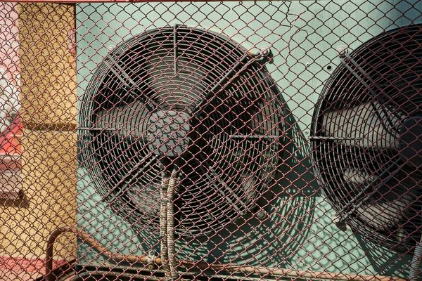 big black fan on the wall behind a gray iron grating