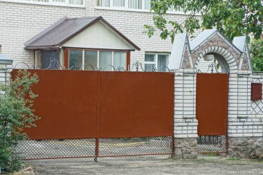 kahverengi metal kapı ve sokağın ortasında bir tuğla çit parçası kapalı