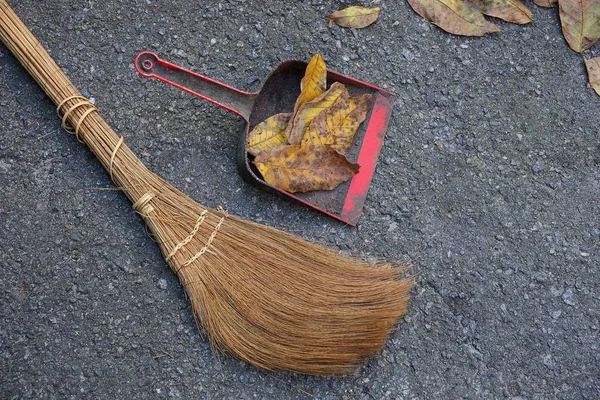 在沥青上的干树叶的棕色扫帚和塑料铲 — 图库照片