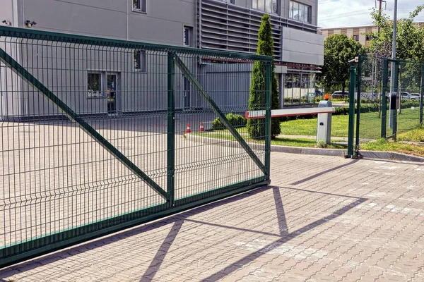 green metal gate and barrier on the sidewalk in front of the industrial building