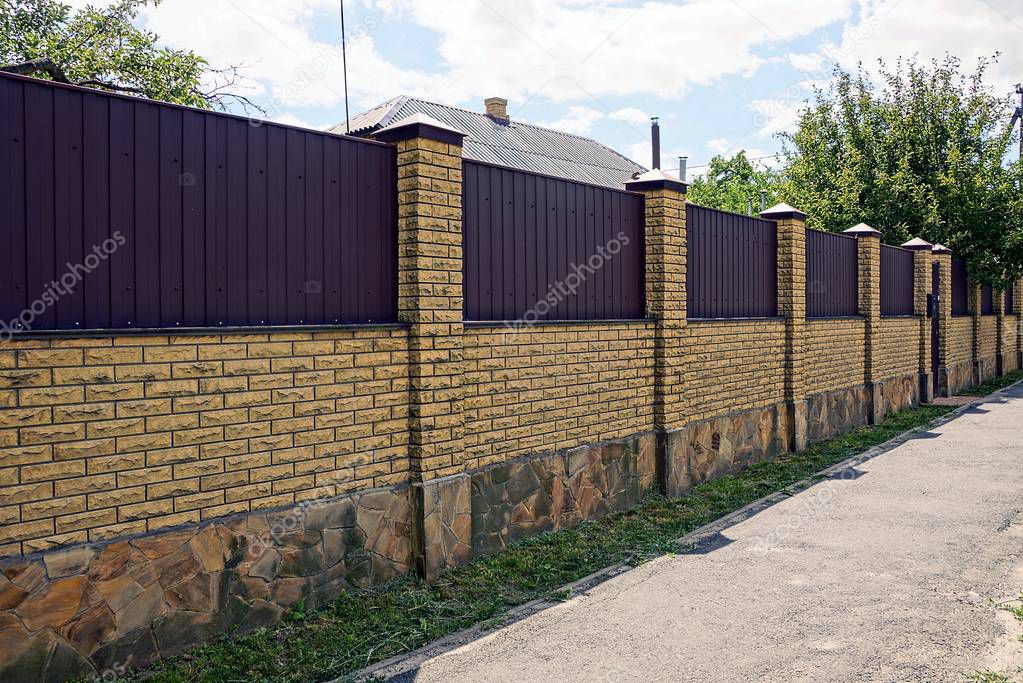 Part of a private iron brown fence and gate at the green grass in the street on a sunny day