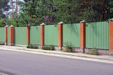Yeşil çit ve kapıları önünde asfalt yol