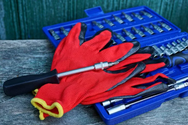 a screwdriver with red work gloves lies on a blue box with a set of tools