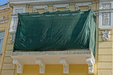 bir binanın duvarına yeşil kumaş kaplı restorasyon altında bir eski balkon
