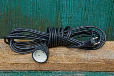 black extension cord in a hank lies on a brown wooden board against a green wall clipart