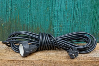 yeşil bir duvara bir kahverengi ahşap masa tahtada bir siyah uzatma kablosu bir hank içinde yatıyor