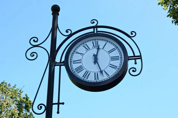 big round clock on a black pillar against a blue sky