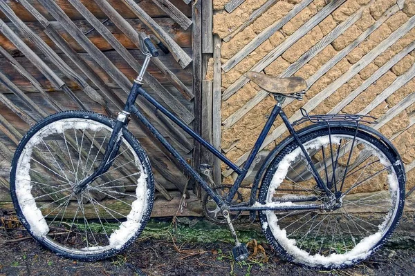 在棕色墙壁附近的雪地里的旧自行车 — 图库照片