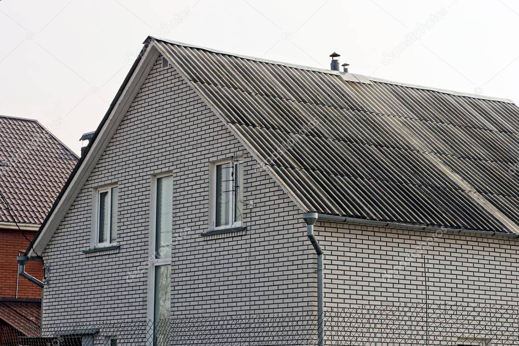 part of a gray brick house with windows under a green tiled roof