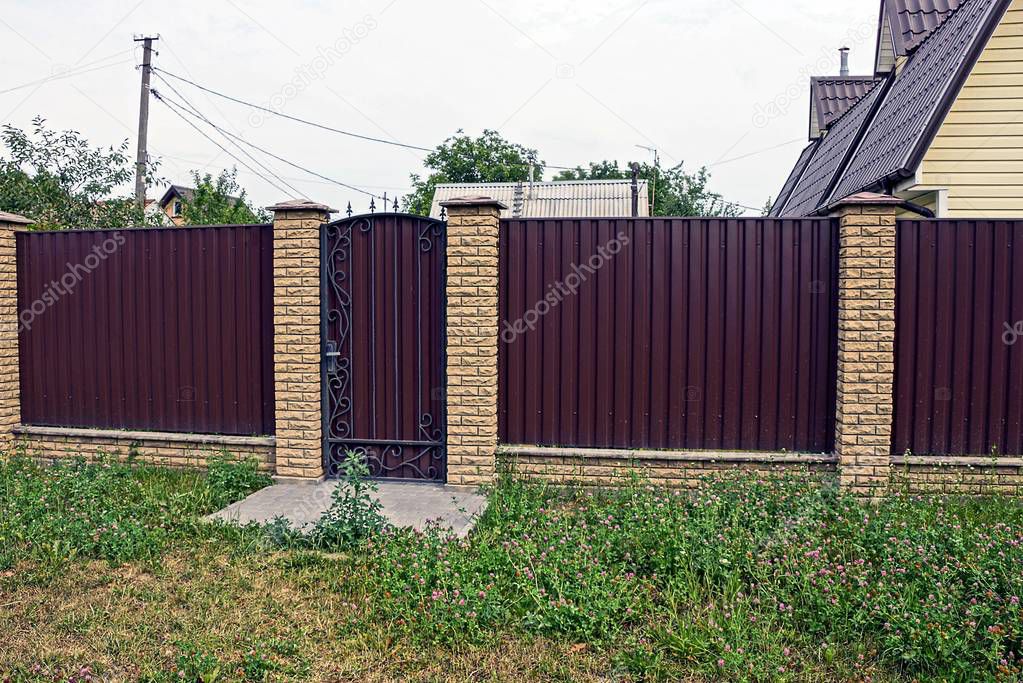 a long brown fence with a closed door of metal and brick outside in the green grass