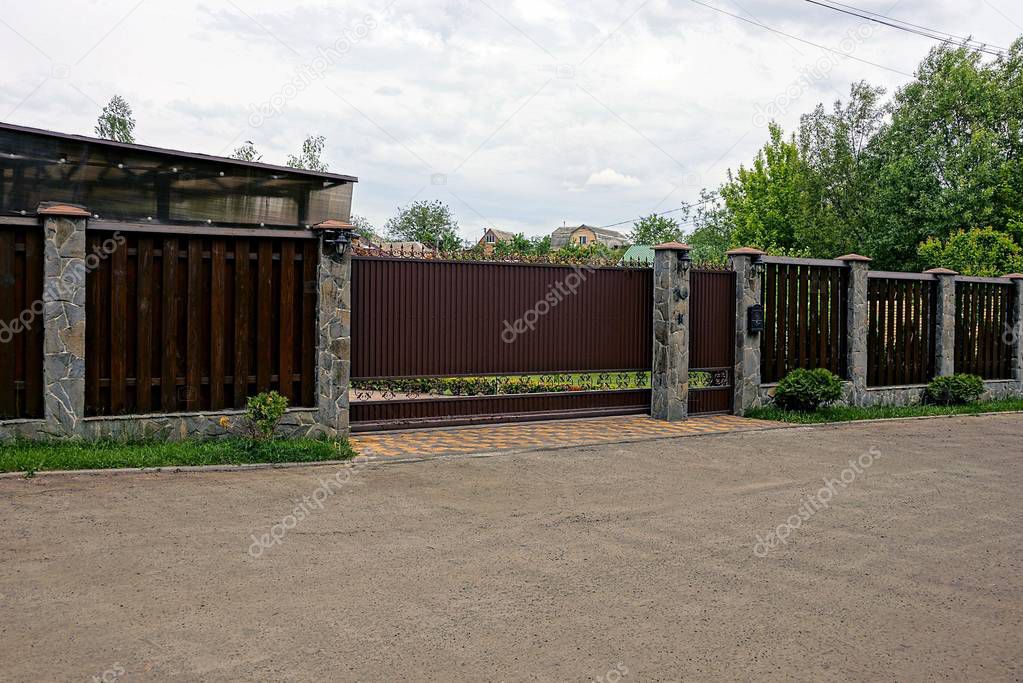 Brown gate and a fence in front of the asphalt road