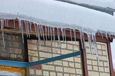 Çatıda bir kahverengi tuğla duvar bir pencere ile kar altında uzun buz sarkıtları satırı