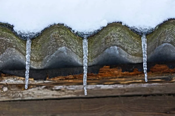 茶色の壁に対して積雪下でスレート屋根の上 つの氷柱 — ストック写真