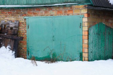 Beyaz kar dışında bir garaj bir tuğla duvara bir yeşil metal geçit