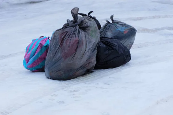 pile of plastic bags with trash on white snow outside