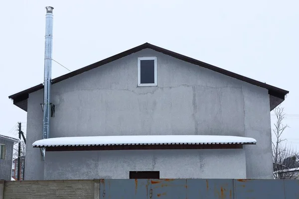 一个灰色的房子的门面 在阁楼上有一个小窗户 栅栏后面的雪下有一个屋顶 — 图库照片