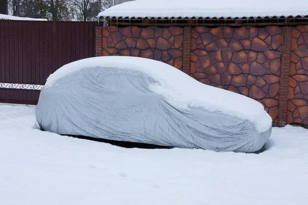 茶色のフェンスの近くに白い雪で車にカバー グレー防水シート — ストック写真