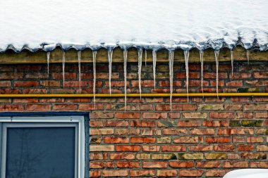 bir tuğla duvar evde bir çatı üzerinden buz sarkıtları satırı