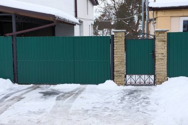 yeşil metal kapılar ve beyaz kar sürüklenir bir kış sokakta bir çit