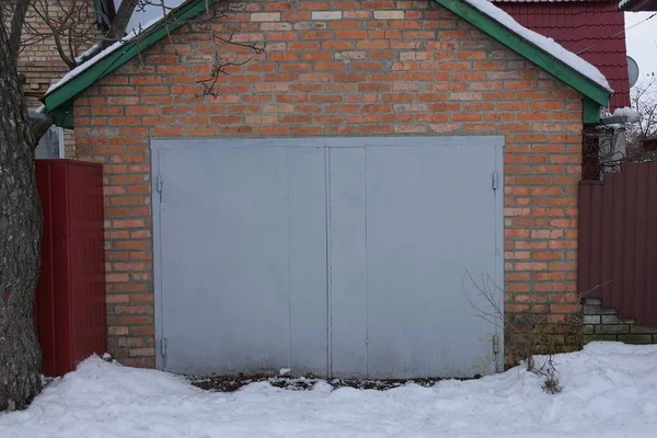 一个封闭的铁灰色大门上的一个棕色砖墙的车库外在白雪 — 图库照片