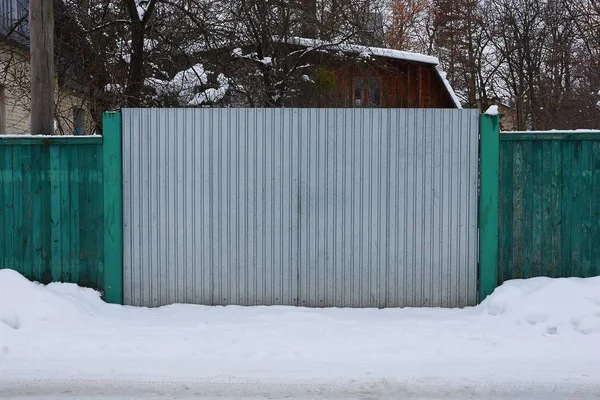 gray metal gates and wooden green fence in the street in white snow