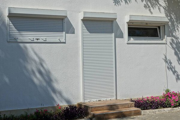 facade of a gray house with windows and a door closed by shutters and a roller shutter