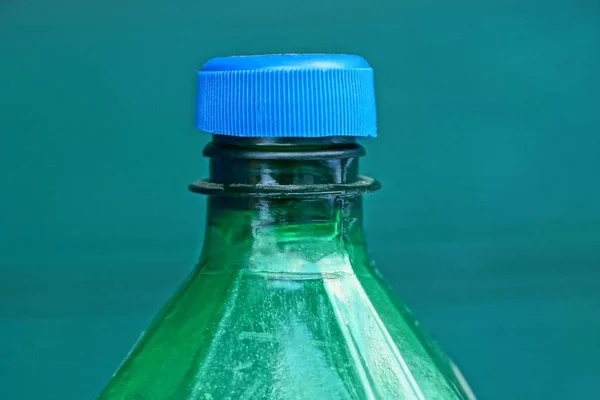 a portion of a large green plastic bottle covered with a blue stopper