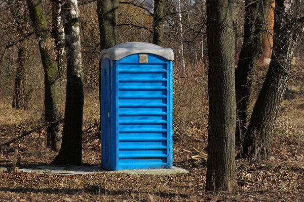 big blue plastic toilet stands among the trees in the park