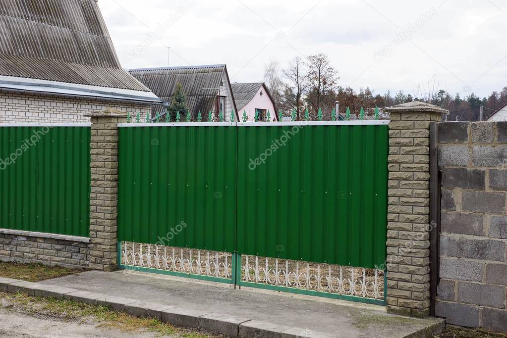 green metal gate and part of a long fence in the street