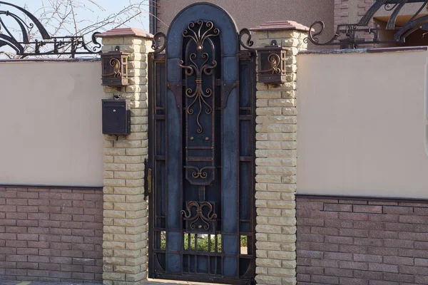 鍛造パターンとレンガとコンクリートで作られたフェンスの一部を持つ茶色の金属製のドア — ストック写真