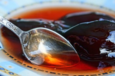 metal bir kaşık ile beyaz bir tabakta kırmızı sıvı erik reçeli