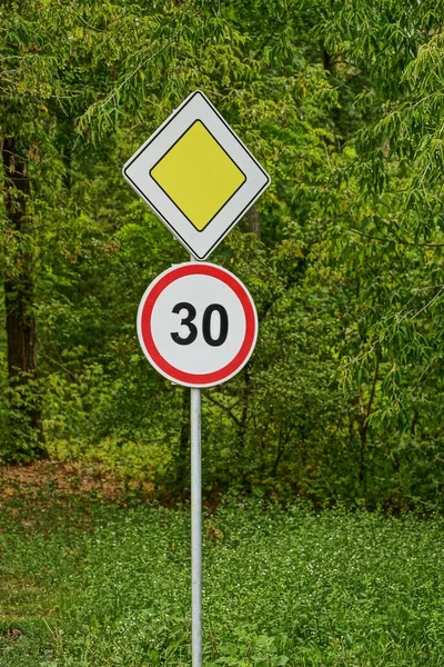 Two road signs near the road against the background of green branches and grass