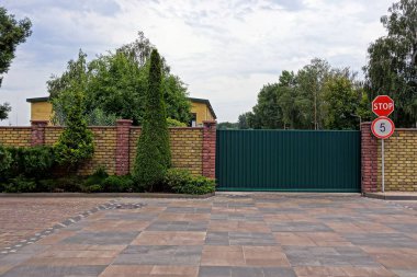 Süs bitkileri ile bir tuğla duvar yakınında yeşil demir kapılar ve yol işaretleri