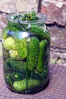 Green cucumbers and seasoning in a glass jar on a brown table