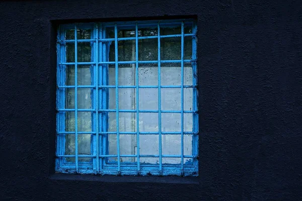 Ein Quadratisches Fenster Hinter Einem Blauen Gitter Einer Schwarzen Betonwand — Stockfoto