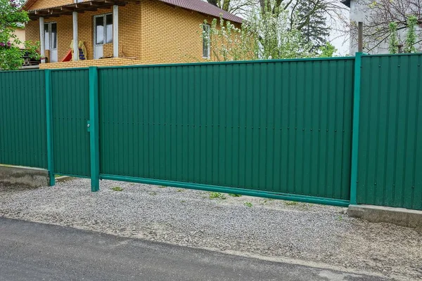 一个长长的绿色金属门和一个农村街道上的栅栏碎片 — 图库照片
