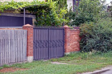 Yeşil bitki örtüsü nde tuğla ve ahşap çit üzerinde demir kapılar