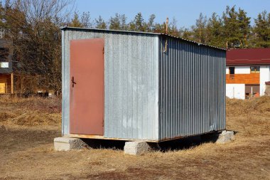 kuru çim dışında duran kahverengi bir kapı ile gri metal römork