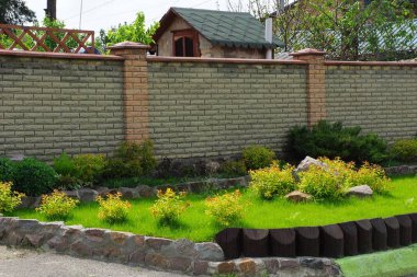 kahverengi bir tuğla çit önünde yeşil çim ve süs bitki örtüsü