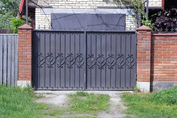 鍛造パターンと緑の草の外側のレンガのフェンスの一部を持つ茶色の金属ゲート — ストック写真