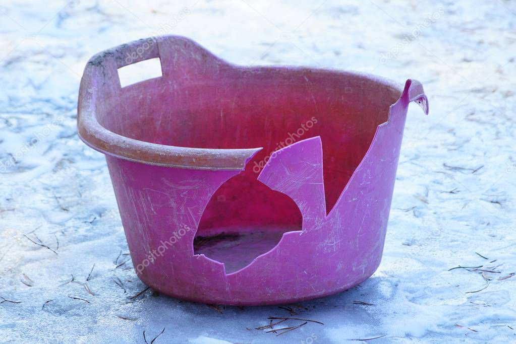 dirty broken red plastic basin stands on the street on white ice