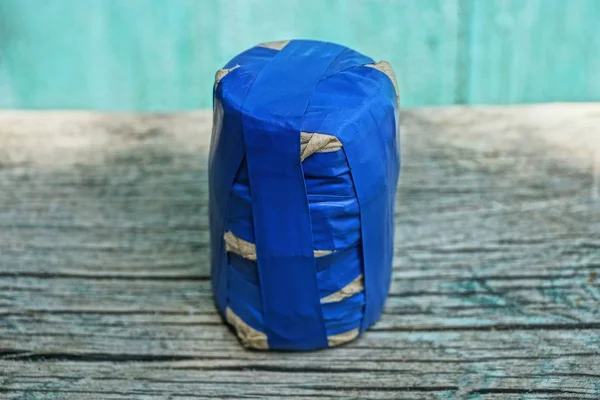 一个用蓝色电带包裹的小盒子躺在绿色背景上的灰色桌子上 — 图库照片