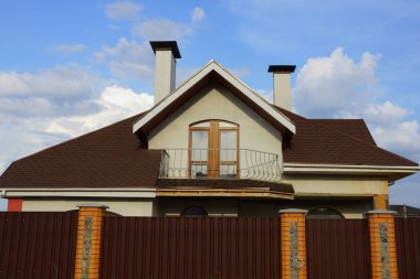 bir çit arkasında kahverengi bir çatı altında bir balkon ile bir evin cephe