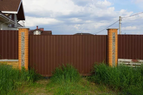 棕色的金属门和栅栏在街上长满了绿草 — 图库照片