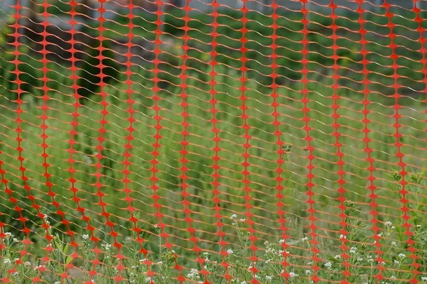 绿草背景上红色塑料网围栏的纹理 — 图库照片