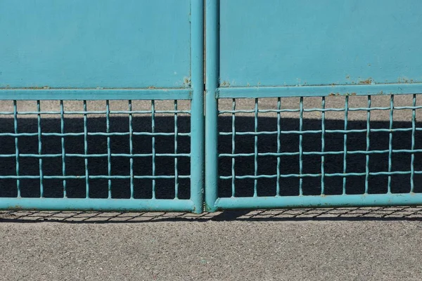 灰色沥青上方金属门上的蓝色铁格栅纹理 — 图库照片