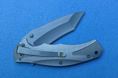 bir siyah metal askeri katlanır bıçak mavi bir masada yatıyor