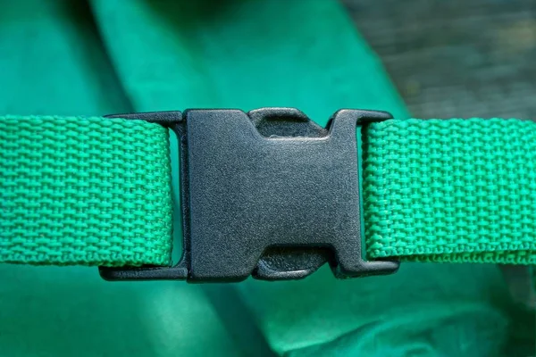 one black carbine latch on the harness on the green matter of the backpack