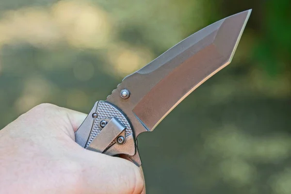 one black folding knife in his hand on a gray background
